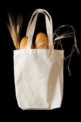 Bread and wheat in a reusable bag against a stark black backdrop creating contrast