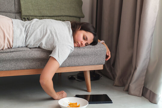 Tired woman lying face-down on a couch at home, feeling exhausted and lacking energy. Concept of fatigue, burnout, stress, low motivation and emotional overload in everyday life.