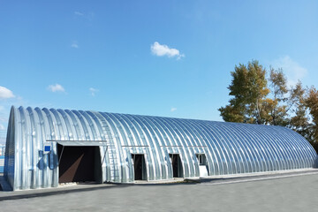 Silver stainless steel hangar with semicircular roof against blue sky background, daytime, sunlight.