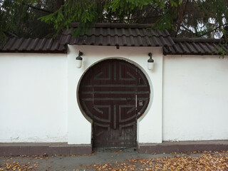 A round antique wooden door set into the wall of a plastered fence. The entrance to the courtyard of a private home.