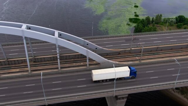 Two freight trucks move in opposite directions along a broad bridge while parallel railway tracks run below the steel arches, forming a clear transport corridor above the river