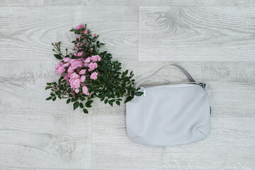 A bouquet of pink garden roses in a white leather bag lying on a white wooden background. Top view.