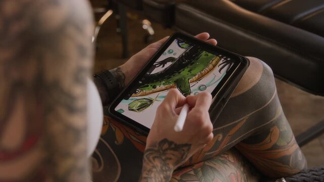 High angle cropped shot of unrecognizable talented female illustrator with tattooed arm and leg drawing on graphic tablet using stylus