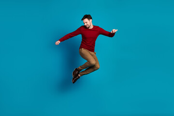 Fototapeta premium Dynamic jump by a young man in red sweater against blue background showcasing casual fashion and athletic style