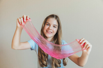 Close-up of hands stretching bright pink slime towards the camera, with a smiling girl in the background. Sensory toy