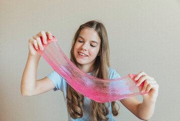 Close-up of hands stretching bright pink slime towards the camera, with a smiling girl in the background. Sensory toy