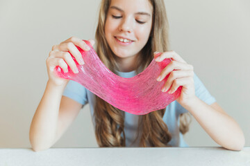 Close-up of hands stretching bright pink slime towards the camera, with a smiling girl in the background. Sensory toy