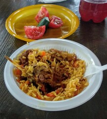 Plate of traditional rice dish with meat and vegetables served alongside fresh tomatoes