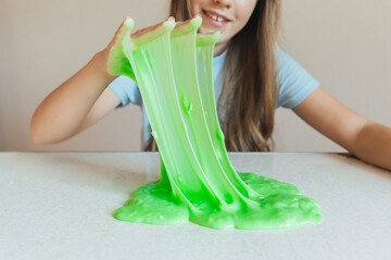 Smiling girl holding and stretching lime green slime wide, showcasing its elasticity and stringy texture. Fun sensory play
