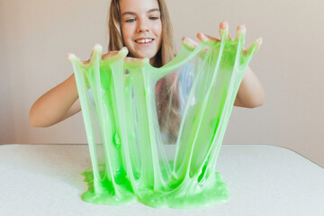 Smiling girl holding and stretching lime green slime wide, showcasing its elasticity and stringy texture. Fun sensory play