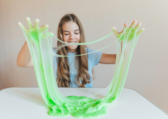 Smiling girl holding and stretching lime green slime wide, showcasing its elasticity and stringy texture. Fun sensory play