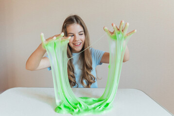 Smiling girl holding and stretching lime green slime wide, showcasing its elasticity and stringy texture. Fun sensory play