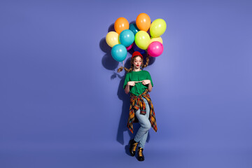Young girl with colorful balloons poses against blue background wearing green shirt jeans and casual jacket for a playful fashion lifestyle stock photo