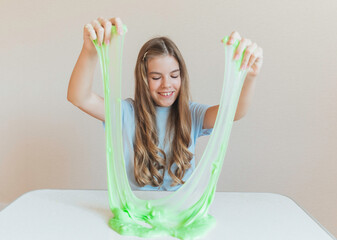 Girl stretching bright neon green slime into a thin translucent sheet on the table. Fun sensory and creative DIY hobby