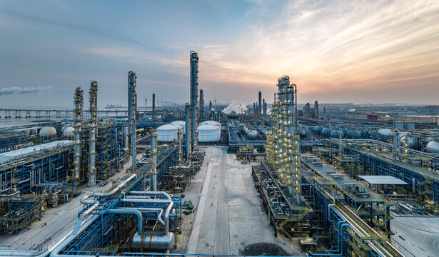 Oil refinery and petrochemical industrial plant with illuminated steel pipelines and towers at sunset.