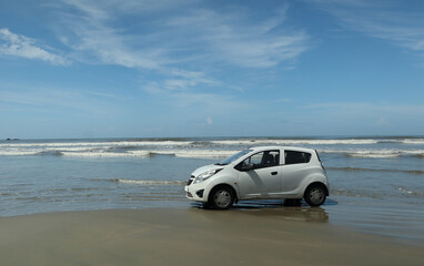 Obraz premium A white motorcar parked on a drive-in beach, picturesque location, sand, sea, ocean water waves and the sky in Kerala, India.