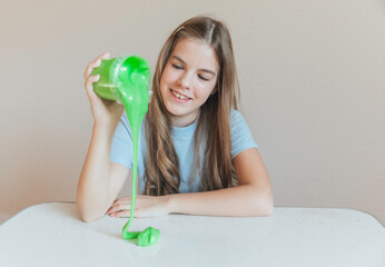 Smiling girl pouring vibrant green slime from a container onto the table. Trendy DIY and fun sensory play activity