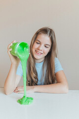 Smiling girl pouring vibrant green slime from a container onto the table. Trendy DIY and fun sensory play activity