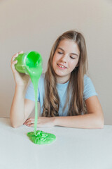 Smiling girl pouring vibrant green slime from a container onto the table. Trendy DIY and fun sensory play activity