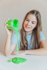 Smiling girl pouring vibrant green slime from a container onto the table. Trendy DIY and fun sensory play activity