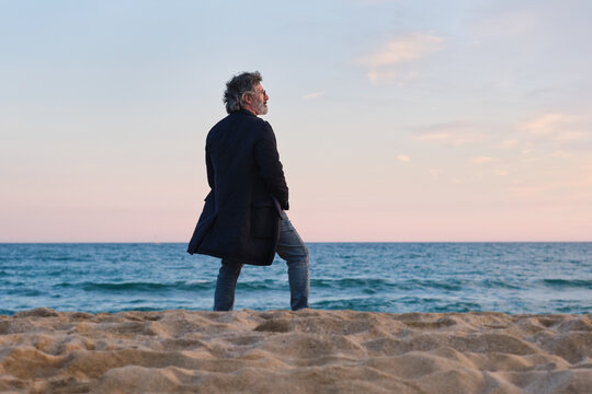 view from behind of Mature man contemplating ocean waves during sunset - Powered by Adobe