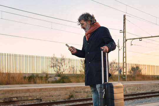 Mature man traveling, smartphone in hand, waiting at train station
