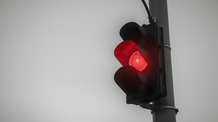 A traffic light showing a bright red light, signaling stop, attached to a pole against a gray sky.