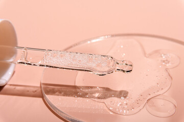 Cosmetic serum  or transparent cosmetic gel falls from the pipette , cosmetic gel textured facial serum on a pink  background