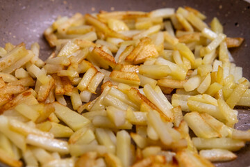 Potatoes cut into slices are deliciously fried in a frying pan.