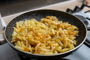 Potatoes cut into slices are deliciously fried in a frying pan.