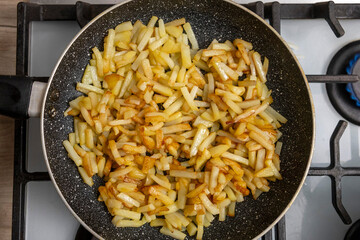 Potatoes cut into slices are deliciously fried in a frying pan.