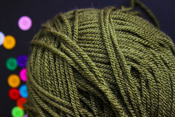Detailed macro of green yarn ball with soft out-of-focus buttons in the background.