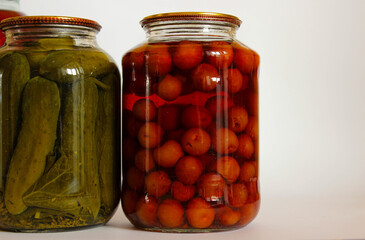 Pair of glass jars with fruit compote and whole pickled cucumbers on a neutral background.
