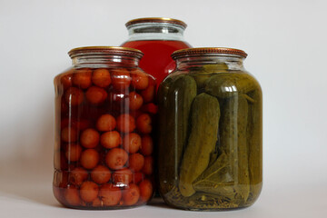 Three large glass jars. fruit compote, pickled cucumbers, and another compote on a white background.