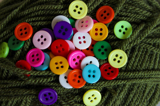 Overhead flat lay of multicolored round buttons resting on green yarn texture.