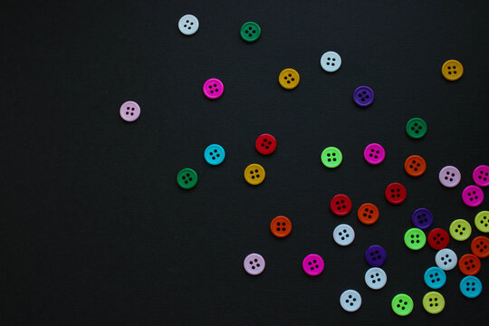 Bright four-hole buttons in many colors scattered across a textured black background.