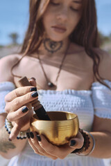 Close up woman begins to play Tibetan bowl with wooden mallet, representing sound healing and meditative focus. Concept of energy of mindfulness and the soothing vibration of inner calm