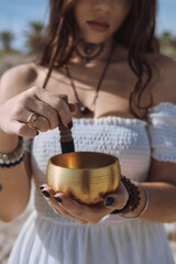 Close up woman begins to play Tibetan bowl with wooden mallet, representing sound healing and meditative focus. Concept of energy of mindfulness and the soothing vibration of inner calm