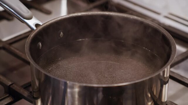 A close-up of steam coming off a boiling pot of water on a clean and modern kitchen stove.