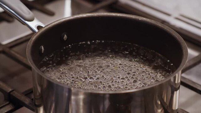 A stainless steel pot filled with freshly boiling water. Bubbles rise to the top of the pot. Heating up the water in preparation for cooking on a modern kitchen stove. Shot in slow motion.