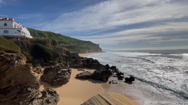 Rocky reef and gentle winter swell roll into a quiet cove beneath white houses in Ca&ntilde;os de Meca