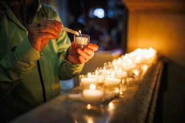 Female worshipper igniting candles in sacred interior of church. Quiet prayer symbolizing christian...
