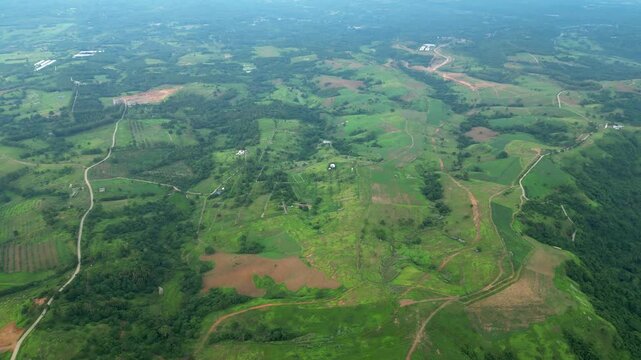 A slow right pan high aerial revealing rolling hills, winding dirt roads, scattered fields, and forest patches, across the rural terrain in Quinawan mountain view, Mariveles Bataan, Philippines