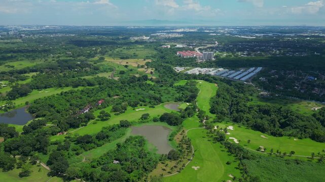 A push aerial moving across manicured fairways and tropical greenery, gradually revealing the distant horizon and urban skyline blending with natural landscapes in Calamba Laguna, Philippines