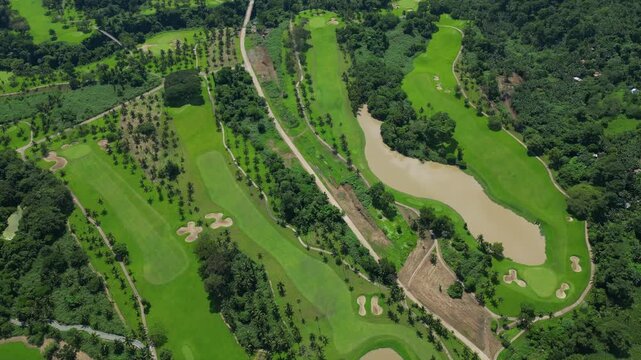 A tilt up aerial rising from manicured fairways and water puddles to reveal tropical greenery, winding paths, and expansive grounds in Canlubang Golf and Country Club, Calamba Laguna, Philippines