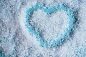 Heart drawn on fluffy white snow. Soft snow texture blue background creates gentle, winter and romantic visual.