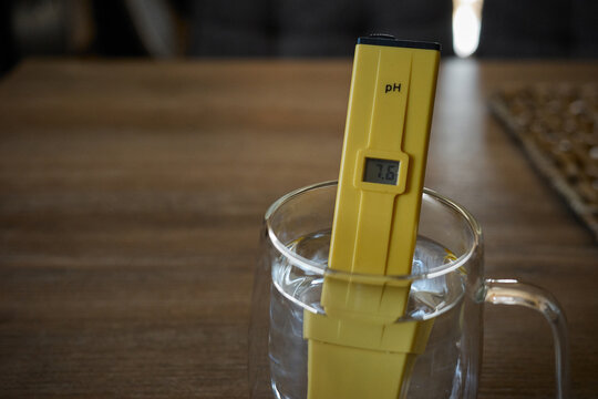 Measurement of water pH level using a digital tester in a clear glass on a wooden table
