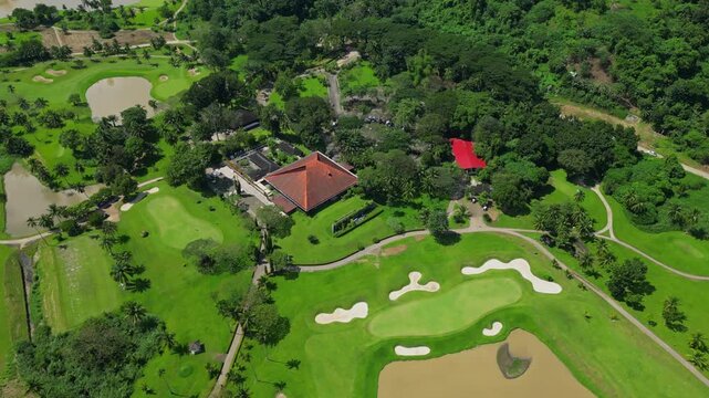 A circling tilt down aerial of the clubhouse and landscaped fairways with water puddles, tropical greenery, and winding paths across Canlubang Golf and Country Club in Calamba Laguna, Philippines