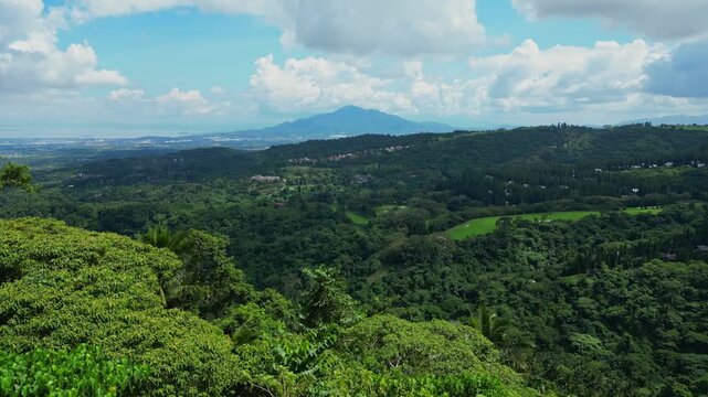 A higher aerial view over forested hills and tropical trees with Mount Makiling visible in the distance under the clouded sky in Calamba Laguna, Philippines