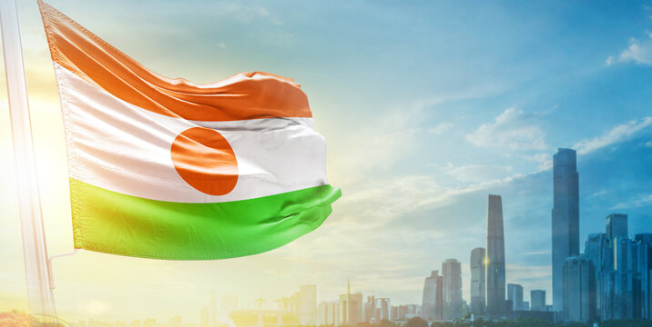 Niger flag wavering in beautiful clouds with building skyline. The flag with drone shot in beautiful sky. Niger national day flag for independence day.